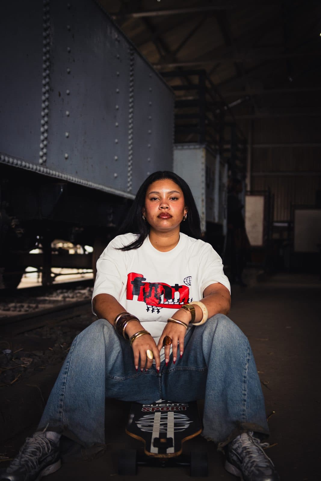 White tee with a crimson block graphic, seated on a skateboard