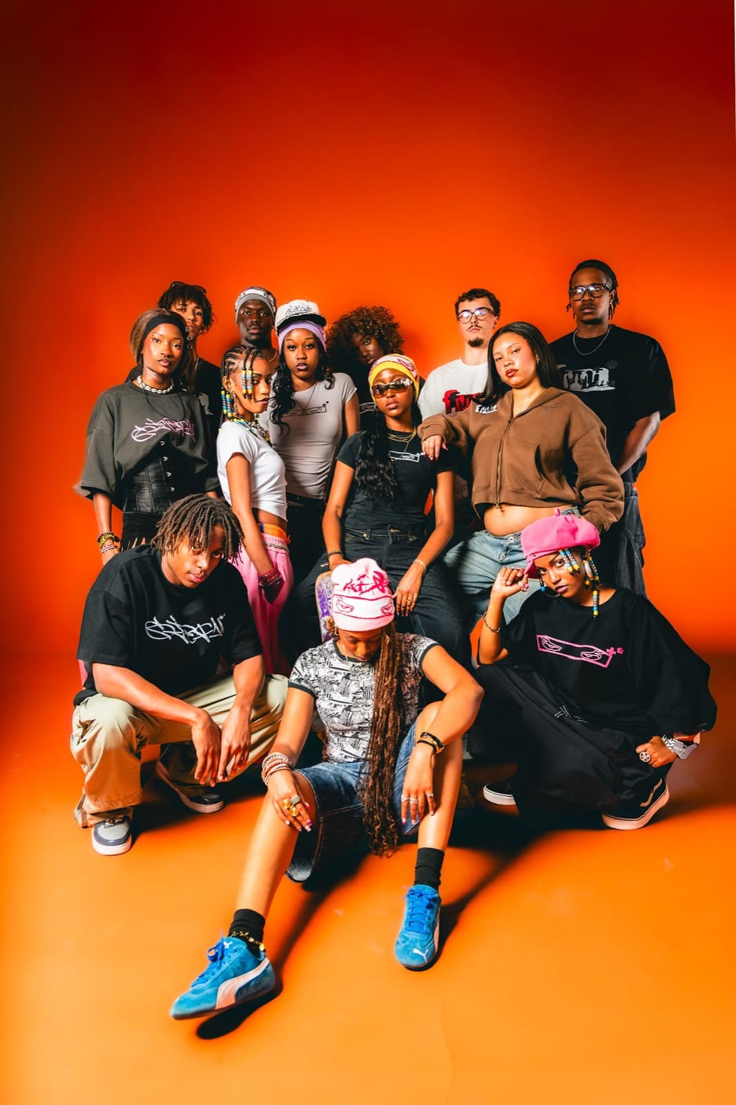 The full fm+ collective on an orange studio backdrop in the Summer 2026 collection.